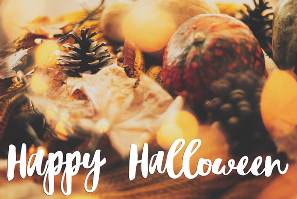 Happy Halloween tekst na dyni, jesienne liście, przyprawy i szyszki sosny na przytulny sweter z dzianiny w ciepłych żółtych świateł, selektywne skupienie. Odręczny znak, sezonowa kartka okolicznościowa - Zdjęcie, obraz