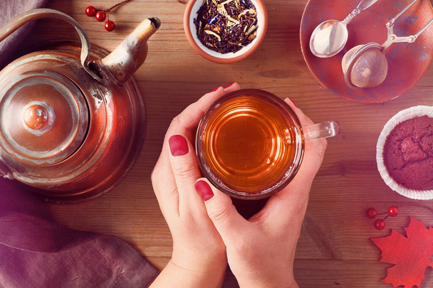 Soğuk bir sonbahar sabahında sıcak bir fincan çay tutan kadın. Antika çaydanlık, çay kaşığı ve kekler.. - Fotoğraf, Görsel