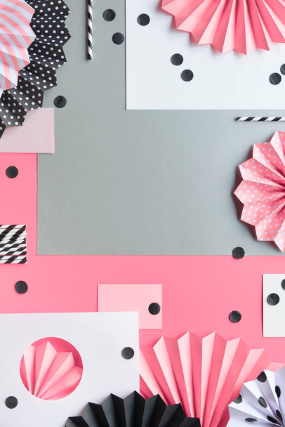 Abstract paper arrangement with circle fans and confetti on pink background. Flat lay with copy-space. Celebration decorations in pink, black and white. Folded paper, drink straws, circles and dots. - Фото, зображення