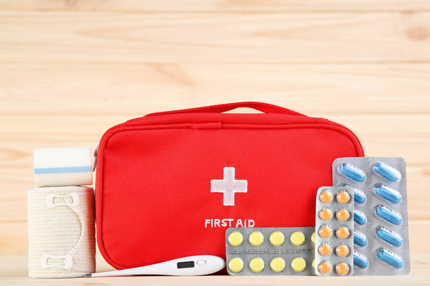 First aid kit with colorful pills, thermometer and bandages on brown wooden table - Photo, Image
