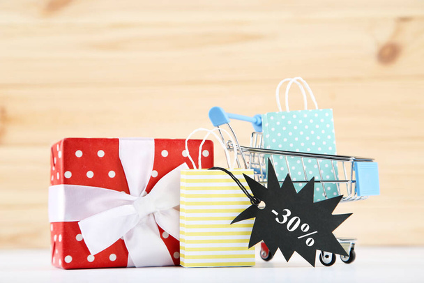 Gift box, shopping cart, black tag and paper bags on wooden background - Valokuva, kuva