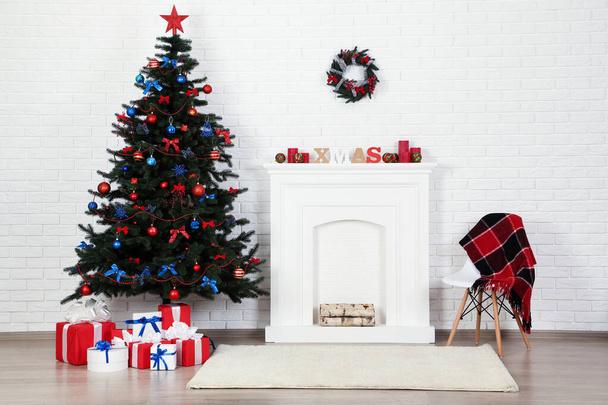 Christmas fir tree with ornaments and gift boxes near decorated fireplace at home - Fotó, kép