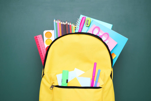 Backpack with school supplies on green background - 写真・画像