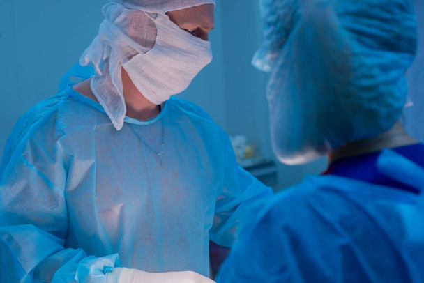 Les chirurgiens pour enfants effectuent des opérations urologiques. Un homme et une femme portant un masque et un manteau bleu stérile dans la salle d'opération. Une équipe de chirurgiens mène une opération. Traitement de la hernie inguinale, œdème testiculaire, maladie testiculaire, varicocelle - Photo, image