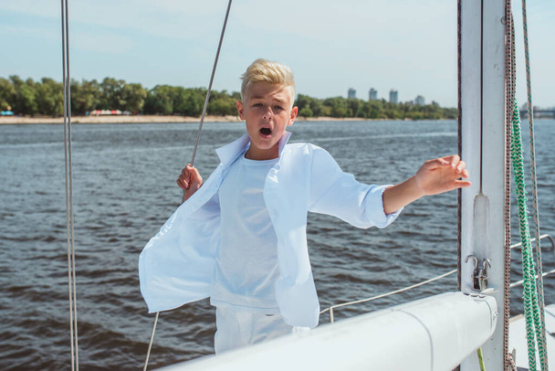 Серьезный молодой симпатичный блондин в белой футболке и рубашке, поющий на яхте. Образование, уроки, учеба, навыки, концепция взросления - Фото, изображение