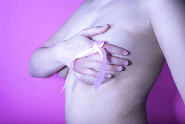 young girl, with a pink ribbon on a finger, on a pink background. Breast cancer concept. - 写真・画像