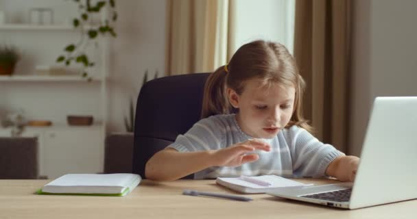 Kleine Schülerin sitzt zu Hause im Quarantäneraum und lernt während der Quarantäne mit Laptop-Online-Fernunterricht. Mutter geht auf Tochter zu, hilft Kind bei Hausaufgaben, unterstützt Kind - Filmmaterial, Video