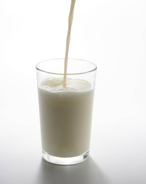 Pouring milk into a glass on white background - Foto, imagen