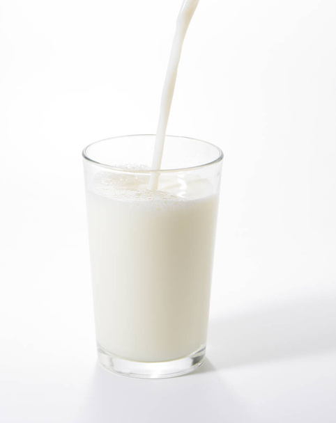 Beyaz arka planda bir bardağa süt dökmek - Fotoğraf, Görsel