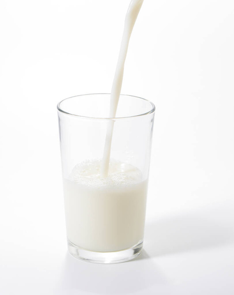 Pouring milk into a glass on white background - Foto, afbeelding