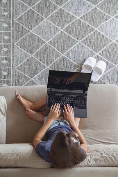 Happy young woman sitting on sofa and using laptop at home. - Foto, Bild