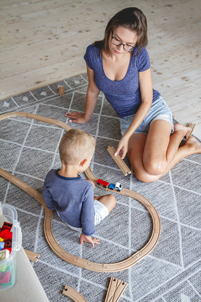 Little kid boy and his mother playing with railway sitting on the floor. - Foto, immagini