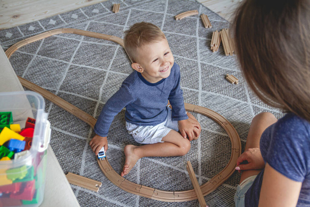 Little kid boy and his mother playing with railway sitting on the floor. - Foto, imagen