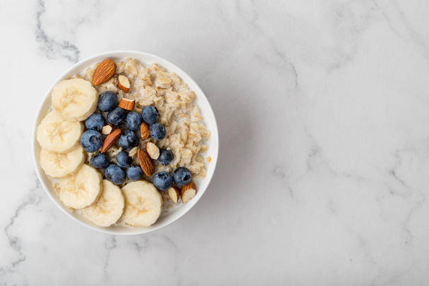 Oatmeal porridge with blueberries, almonds and banana on marble table - Фото, зображення