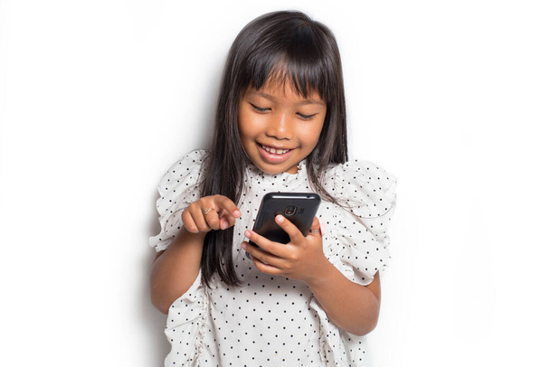 gelukkig aziatische kleine meisje met behulp van smart phone op witte achtergrond - Foto, afbeelding