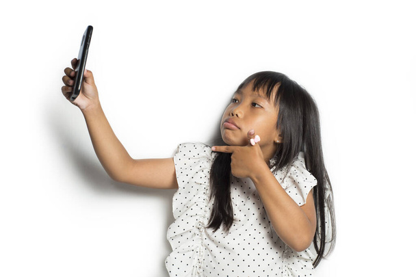 Милая азиатская девочка делает селфи со смартфоном на белом фоне - Фото, изображение