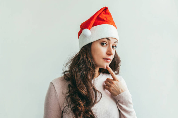 Kırmızı Noel Baba şapkalı güzel kız beyaz arka planda izole edilmiş mutlu ve heyecanlı görünüyor. Genç kadın portresi, gerçek duygular. Mutlu Noeller ve yeni yıl tatili - Fotoğraf, Görsel