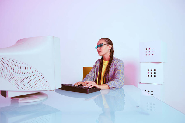 Stylish asian female office worker or hacker in sunglasses typing at obsolete computer. Colored Neon light - Photo, image