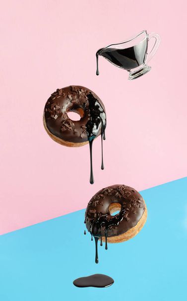 Donuts voladores con chocolate goteando sobre fondo azul rosado. Diseño de arte pop - Foto, imagen