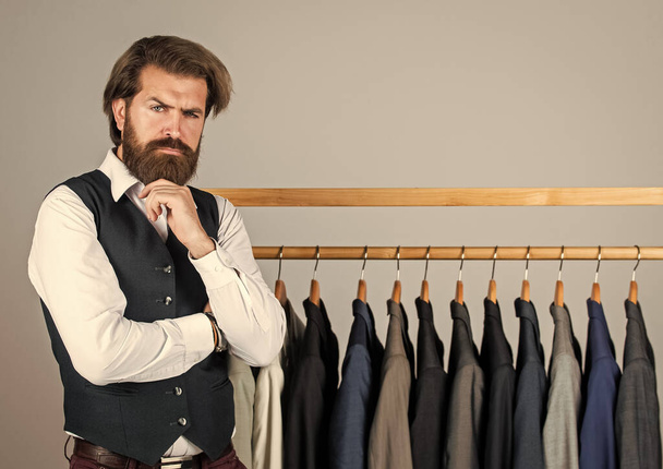Man clothing in boutique. Man with suit. tailor in his workshop. Handsome bearded fashion man in classical costume suit. Man in custom tailored suit presenting expensive tuxedo. Another client - Фото, изображение