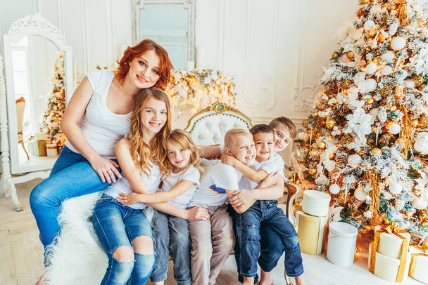幸せな家族の母親と5人の子供はクリスマスの前夜にクリスマスツリーの近くで遊んでリラックスします。冬の装飾が施された明るい部屋にいる母親、娘、息子。クリスマスお祝いのための新年の時間 - 写真・画像