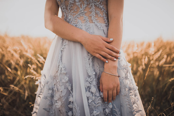meisje in een grijze jurk met bloemen toont haar mooie blauwe manicure - Foto, afbeelding