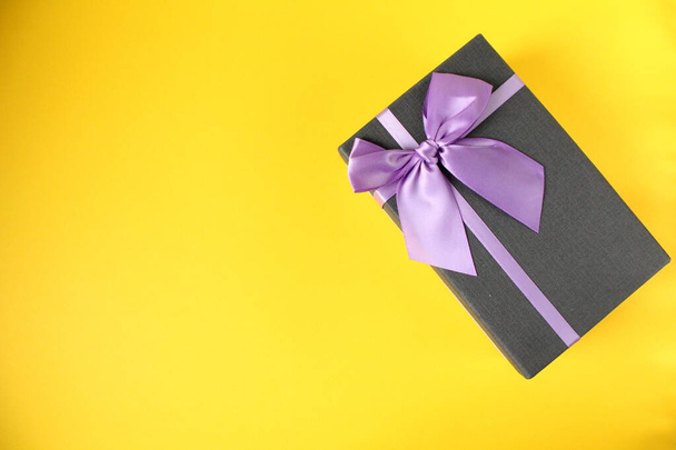 Nieuwjaar Kerstmis verjaardag moederdag vakantie achtergrond cadeau doos zwart cadeau doos met paars paars fuchsia lint en strik op gele achtergrond minimalisme top view met kopieerruimte - Foto, afbeelding
