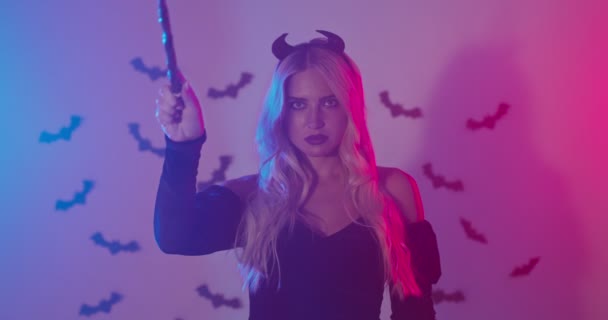 Geheimnisvolle Frau im Halloween-Kostüm und mit Zauberstab gestikulierenden Hörnern, verrauchtes Studio mit Neonlicht - Filmmaterial, Video