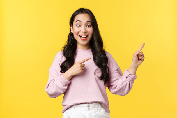 People emotions, lifestyle and fashion concept. Smiling female student showing summer vacation offers, special promo or discounts at store, pointing fingers right and smiling, yellow background - Photo, Image