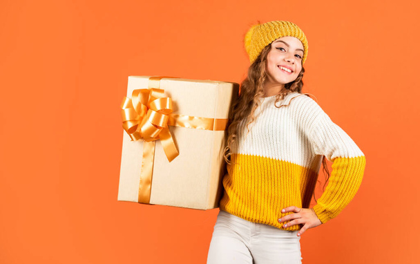 Find presents online. gift delivery service. shopping advantages. christmas is here. winter holiday surprise. girl knitted hat and sweater. kid hold present box orange background. happy new 2020 year - Fotografie, Obrázek