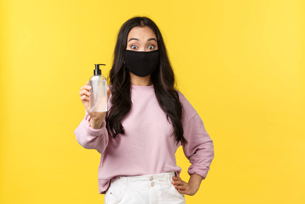Covid-19, social-distancing lifestyle, prevent virus spread concept. Surprised asian girl in face mask always using hand sanitizer during coronavirus pandemic, recommend hygiene product - Photo, Image