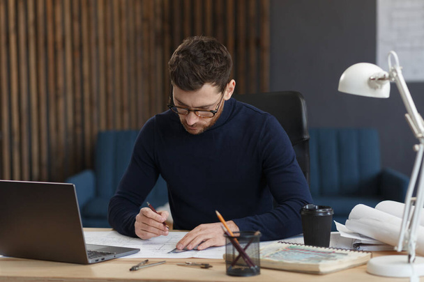 Architect working in office with blueprints.Engineer inspect architectural plan, sketching a construction project.Portrait of handsome bearded man sitting at workplace. Business construction concept - Fotó, kép