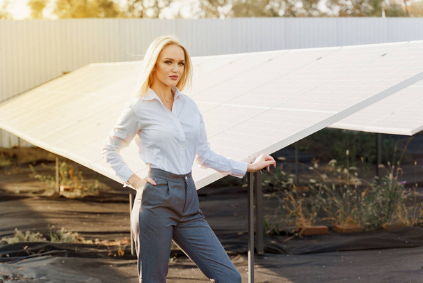 Meisje staan en kijk rechts in de buurt van zonnepanelen rij op de grond met zonlicht. Vrouwelijke investeerder draagt formeel wit shirt. Gratis elektriciteit voor thuis. Duurzaamheid van de planeet. Groene energie. - Foto, afbeelding