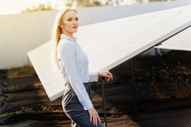 Güneş panellerinin yanında duran kız yerde güneş ışığıyla kürek çekiyor. Kadın yatırımcı resmi beyaz gömlek giyer. Ev için bedava elektrik. Gezegenin sürdürülebilirliği. Yeşil enerji. - Fotoğraf, Görsel