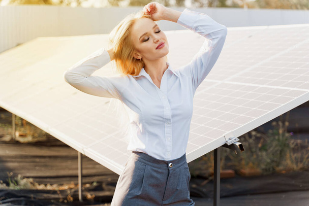 Mädchen stehen und schauen bei Sonnenuntergang rechts zwischen 2 Sonnenkollektoren auf dem Boden. Investorin trägt formell weißes Hemd. Kostenloser Strom für zu Hause. Nachhaltigkeit des Planeten. Grüne Energie. - Foto, Bild