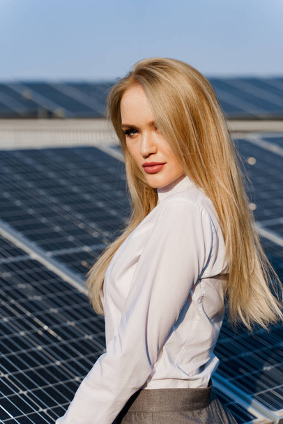 Nahaufnahme Porträt eines blonden Models in der Nähe von Sonnenkollektoren. Frau trägt weißes Hemd am Kraftwerk. Kostenloser Strom für zu Hause. Grüne Energie. Solarzellen-Kraftwerksgeschäft. - Foto, Bild