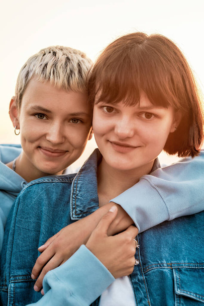 Portrét dvou atraktivních mladých žen s krátkými vlasy s úsměvem na kameru, Mladé lesbičky pár tráví čas spolu, objímání při pózování venku - Fotografie, Obrázek