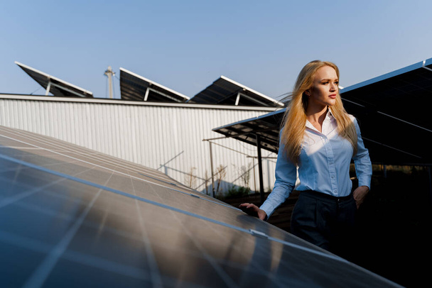 女の子は日没時に地面に2枚のソーラーパネルの列の間を歩く。女性投資家は正式な白いシャツを着ている。家のための無料電気。地球の持続可能性。緑のエネルギー. - 写真・画像