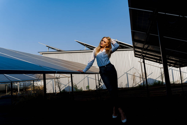 Девушка ходит между двумя солнечными панелями ряд на земле на закате. Женщина-инвестор носит официальную белую рубашку. Бесплатное электричество для дома. Устойчивость планеты. Зеленая энергия. - Фото, изображение