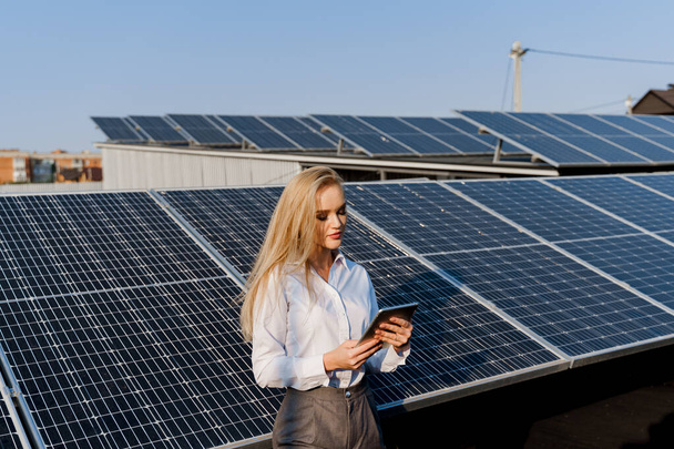 Investor woman stand with tablet near blue solar panels row on the ground Girl weared formal white shirt. Free electricity for home. Sustainability of planet. Green energy. - Фото, изображение