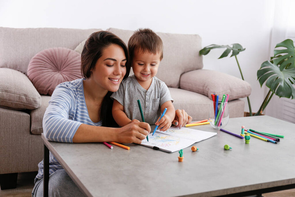 Young beautiful woman teaching her two year old son to draw at home. Woman spending quality time with her toddler child. Close up, copy space, background. - Foto, immagini
