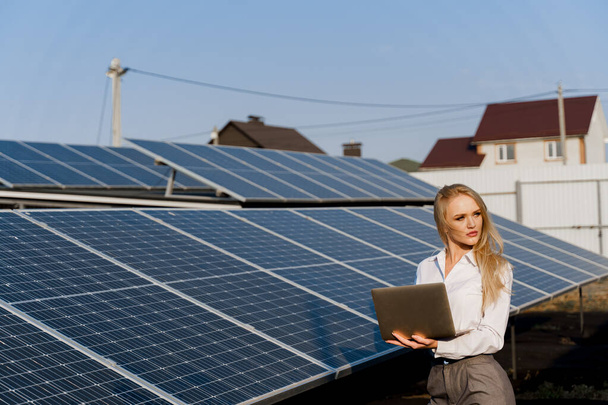 Investor und Sonnenkollektoren. Blonde Frau mit Laptop in der Nähe blauer Sonnenkollektoren reiht sich auf dem Boden. Kostenloser Strom für zu Hause. Nachhaltigkeit des Planeten. Grüne Energie. - Foto, Bild