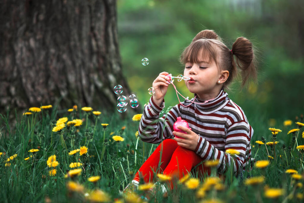 Kleines süßes Mädchen bläst Seifenblasen im Park. - Foto, Bild