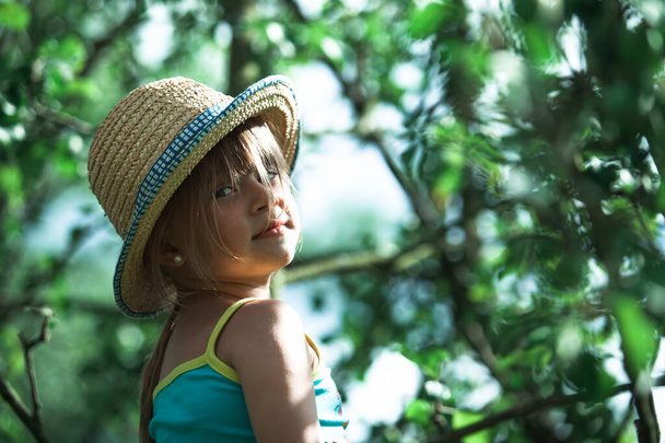 Little girl is sitting in the branches of an green tree. - Foto, Bild