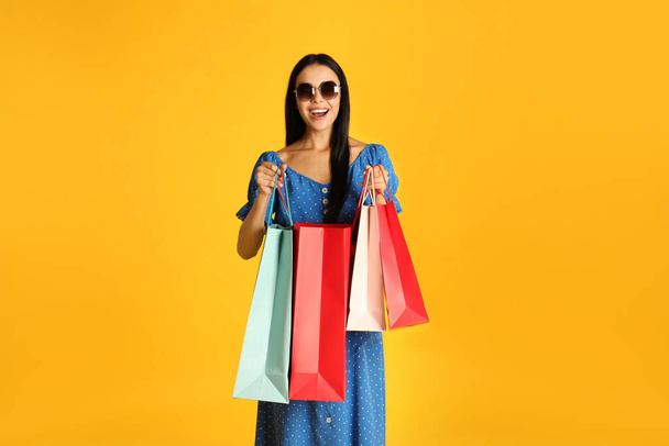 Beautiful young woman with paper shopping bags on yellow background - Photo, Image