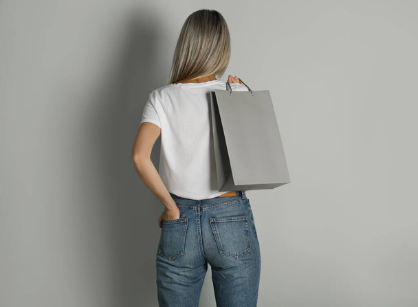 Mujer con bolsa de papel sobre fondo gris claro, vista trasera - Foto, Imagen