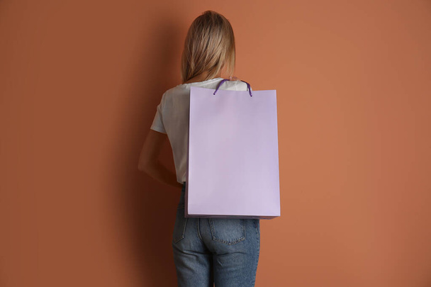 Woman with paper shopping bag on light brown background, back view - Fotó, kép