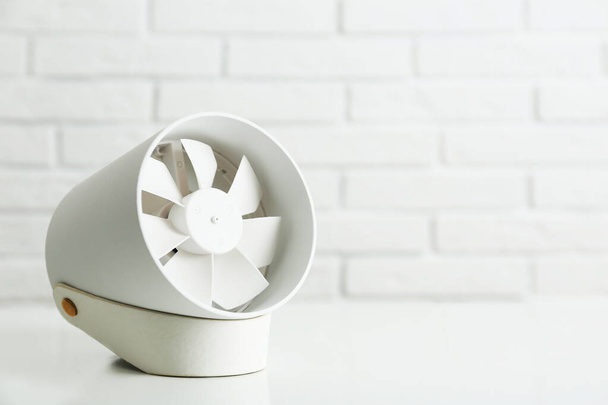 Portable fan on table near white brick wall, space for text. Summer heat - 写真・画像
