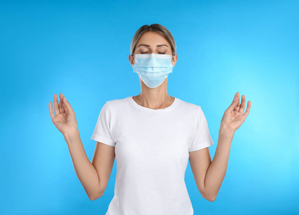 Woman in protective mask meditating on light blue background - 写真・画像