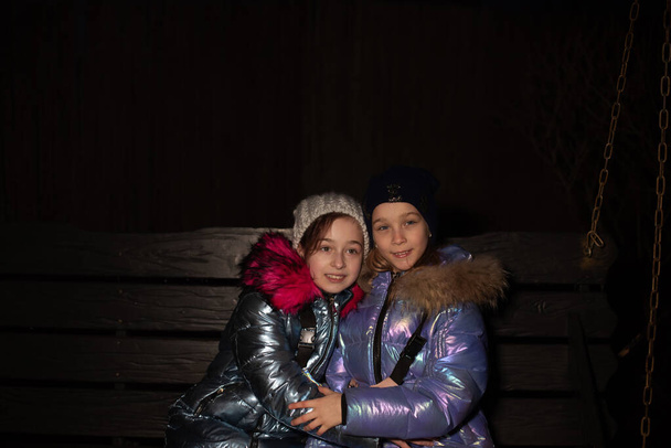 Two young beautiful girlfriends walk in the winter. Two teenage girlfriends in winter jackets - Photo, Image